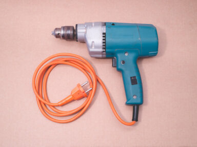 Vintage blue electric drill from the seventies with curled up orange cord, captured from above on a pink background.  Get this digital image in high resolution for print or other purposes.  All prices excluding VAT. You may be charged VAT depending on your region (if you are from the EU for example).