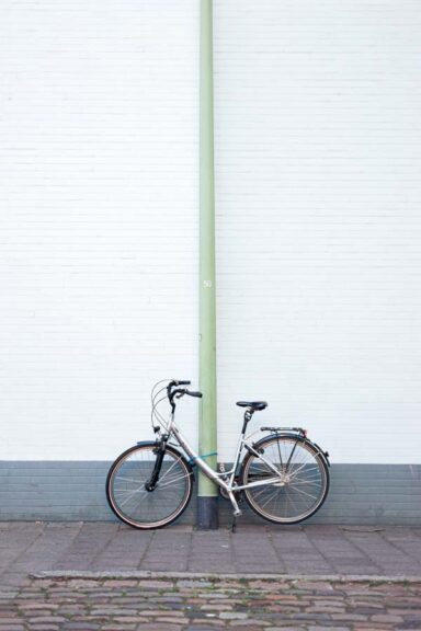Discover the beauty of simplicity with this stunning digital photo of a single bicycle, securely locked to a vibrant green street lamp post. The bike stands tall against the backdrop of a towering building wall, creating a striking contrast that draws the eye towards the center of the image. Capturing the essence of minimalism, this photograph showcases the elegance and grace of everyday objects in their natural environment. Perfect for printing and displaying in any modern space, this image is sure to inspire and delight all who view it.