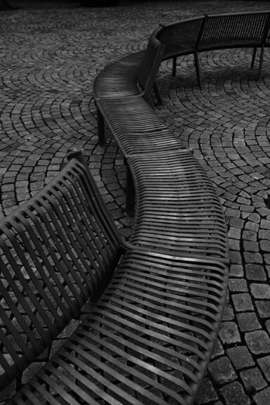 A very long curvy metal bench outside the Morgestern Museum in Bremerhaven, Germany, in black&white. This unsusual bench is an estimated 50 meters long and covers in its whole length the entirety of a parking lot sized resting area. Get this digital image in high resolution for print or other purposes. All prices excluding VAT. You may be charged VAT depending on your region (if you are from the EU for example).